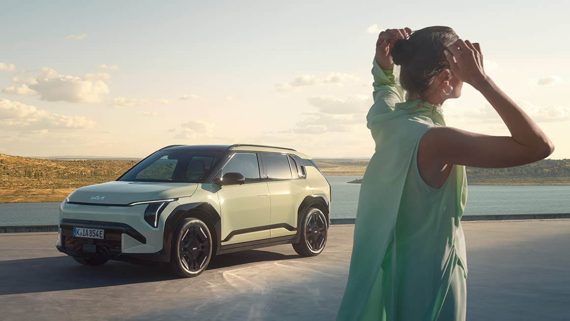 Der neue Kia EV3, Frau steht vor Fahrzeug in weiter Landschaft