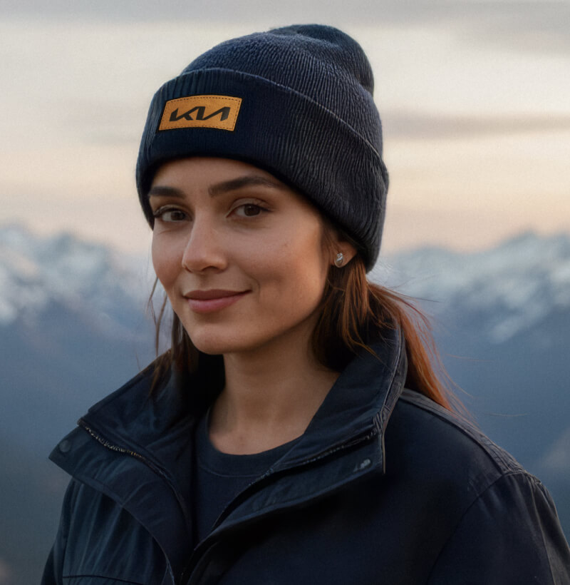 Woman is wearing the Kia Beanie from the Kia Collection in front of snow covered mountains.